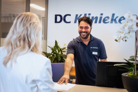 A smiling man with dark hair and a beard, wearing a navy blue polo shirt with 