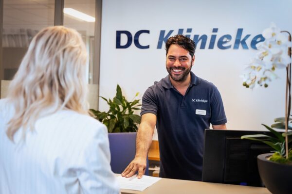 A smiling man with dark hair and a beard, wearing a navy blue polo shirt with 